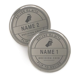 Puede incluir: Dos monedas de decisi&oacute;n plateadas. Cada moneda tiene un nombre, "NAME 1" y "NAME 2", en una fuente sans-serif. Las monedas tienen las palabras "FLIP TO DECIDE" alrededor del borde y un gr&aacute;fico de mano. Tambi&eacute;n est&aacute;n presentes las palabras "DECISION COIN".