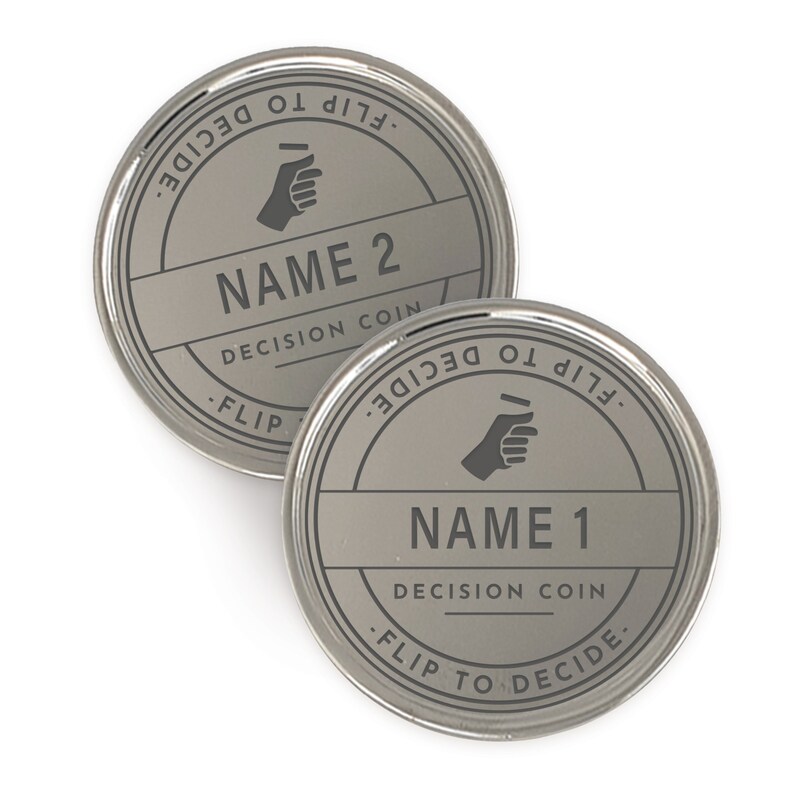 Puede incluir: Dos monedas de decisi&oacute;n plateadas. Cada moneda tiene un nombre, "NAME 1" y "NAME 2", en una fuente sans-serif. Las monedas tienen las palabras "FLIP TO DECIDE" alrededor del borde y un gr&aacute;fico de mano. Tambi&eacute;n est&aacute;n presentes las palabras "DECISION COIN".