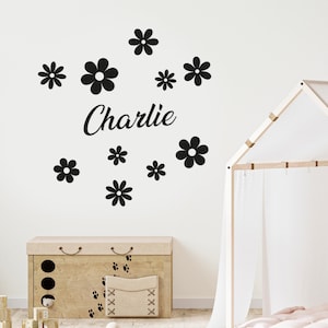 Puede incluir: Pegatina de pared en blanco y negro con el nombre "Charlie" y una dispersi&oacute;n de peque&ntilde;os dise&ntilde;os de flores.