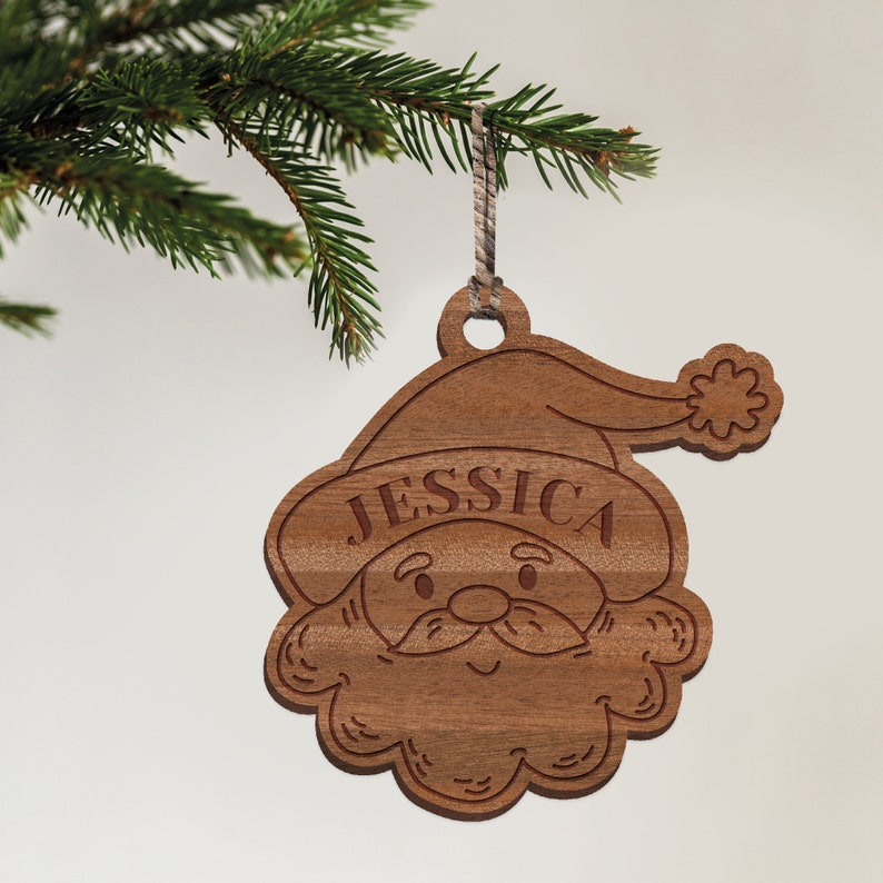 May include: A wooden Christmas ornament shaped like Santa Claus with the name "JESSICA" engraved on the hat. The ornament is brown and has a white string for hanging.