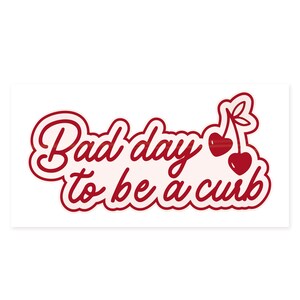 K&ouml;nnte beinhalten: Rechteckiger Aufkleber mit dem Schriftzug "Bad day to be a curb" in roter Schreibschrift. Zwei rote Kirschen mit gr&uuml;nen Stielen befinden sich auf der rechten Seite. Der Hintergrund ist wei&szlig;.