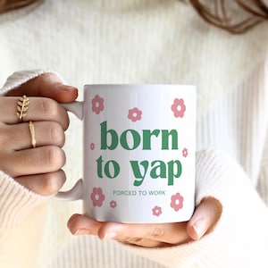May include: White ceramic mug with green text that reads "born to yap" and smaller text that reads "forced to work". The mug is decorated with pink flowers.