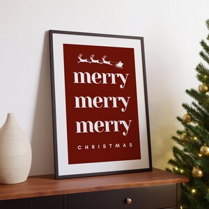 May include: Framed Christmas art print with a red background and white text. The words "merry merry merry" are stacked vertically, with "CHRISTMAS" below. A white silhouette of Santa's sleigh and reindeer is at the top.