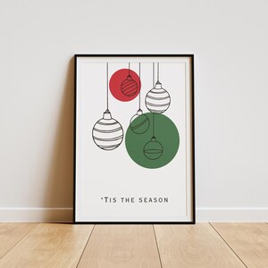 K&ouml;nnte beinhalten: Ein druckbarer Kunstdruck mit einem minimalistischen Design, das vier Weihnachtskugeln zeigt, die an Schn&uuml;ren h&auml;ngen. Die Kugeln sind wei&szlig; mit schwarzen Streifen und in einem Kreis angeordnet, hinter dem sich ein roter und ein gr&uuml;ner Kreis befinden. Der Text 'Tis the Season ist unter den Kugeln gedruckt.