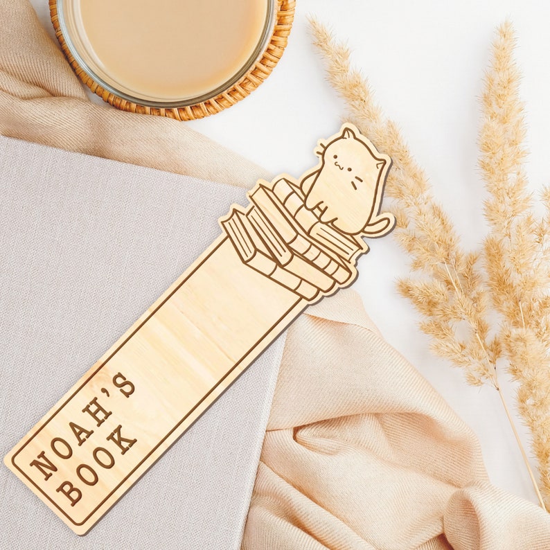 May include: A wooden bookmark with a cat sitting on top of a stack of books. The bookmark is engraved with the text "Noah's Book".