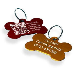 May include: Two dog bone-shaped pet ID tags. One is red with a QR code and the text "Scan me with your phone camera or QR Code Scanner on Apple". The other is gold with the text "I'm Lost! Call my parents 07123 456789".
