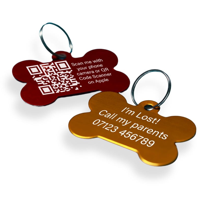 May include: Two dog bone-shaped pet ID tags. One is red with a QR code and the text "Scan me with your phone camera or QR Code Scanner on Apple". The other is gold with the text "I'm Lost! Call my parents 07123 456789".