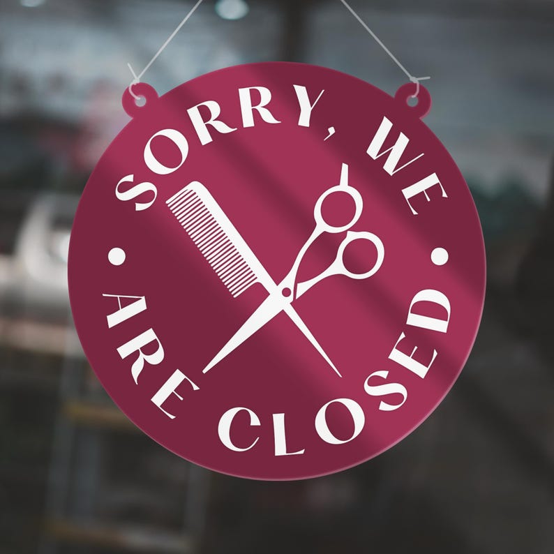 May include: A round, burgundy sign with white text and a white comb and scissors graphic. The sign reads "SORRY, WE ARE CLOSED" in a circular arrangement, indicating a closed business, likely a salon or barber shop.