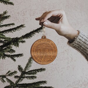 May include: A wooden Christmas ornament with the text "Christmas in our home 2023" and a stylized image of a house with a window and a moon above it.