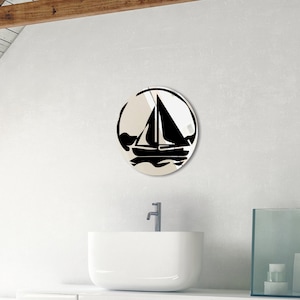May include: A round mirror with a black silhouette of a sailboat on a white background. The mirror is hanging on a white wall above a white sink.