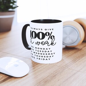 May include: White ceramic mug with a black interior and handle. The mug has black text that reads "I always give 100% at work" and a list of days of the week with percentages next to them.