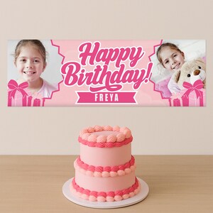 May include: A pink birthday banner with the text "Happy Birthday!" and the name "Freya". The banner has photos of a girl and gift boxes. A two-tiered pink cake with decorative frosting sits below.