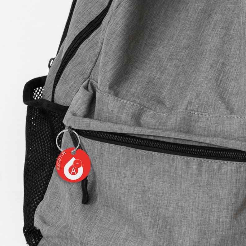 May include: A gray backpack with a black zipper and a red blood type keychain with a white letter A and the words "BLOOD TYPE" on it.