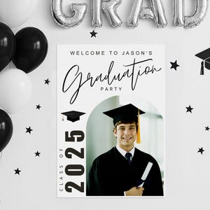 May include: A graduation party sign with the text "Welcome to Jason's Graduation Party" and "Class of 2025". The sign features a photo of a graduate in a cap and gown, with black and white balloons and star decorations.