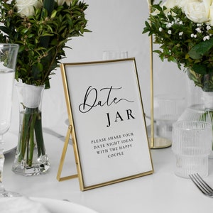 May include: Gold-framed sign with the text "Date JAR" and the message "Please share your date night ideas with the happy couple".
