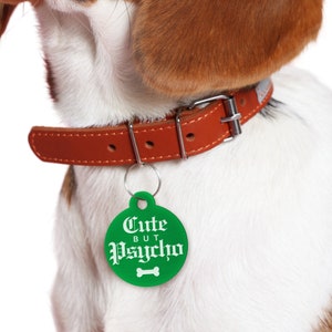 May include: A brown leather dog collar with a green tag that reads "Cute But Psycho" in white gothic font. The tag has a white bone icon.