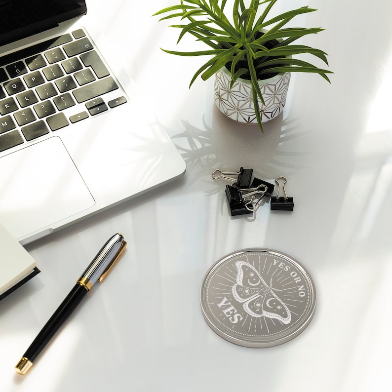 May include: A silver-colored, round, decorative coaster with a black and white illustration of a moth with the words "YES OR NO" and "YES" printed on it.