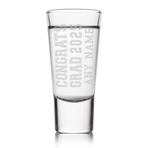 May include: A clear shot glass with the words "CONGRATS GRAD 2023 ANY NAME" etched in a bold, sans-serif font. The glass is filled with a clear liquid, and the design is centered on the glass.