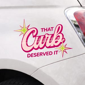 May include: A pink and light pink car decal with the text "THAT Curb DESERVED IT" in a retro font, accented with starburst graphics. The decal is applied to a white car.