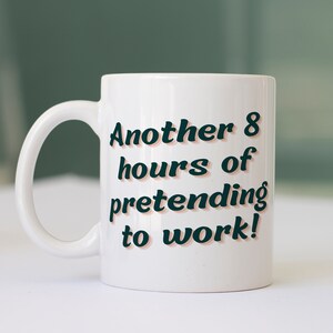 Puede incluir: Taza de cer&aacute;mica blanca con un dise&ntilde;o en negro y naranja. El texto en la taza dice "Another 8 hours of pretending to work!"