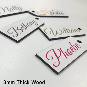 May include: Six white wooden gift tags with black edges. The tags are personalised with names in different colours: "Matty", "Krislie", "Bethany", "William", "Phoebe". The tags are 3mm thick wood.