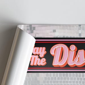 Pu&ograve; includere: Un poster con le parole "Stay The Disco" in lettere rosa e arancioni su sfondo nero. Il poster ha uno sfondo di piastrelle argentate e un bordo bianco arricciato.