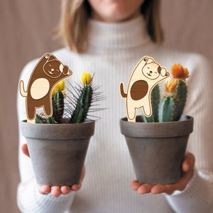 May include: Two brown terracotta pots with cactus plants and wooden dog figurines. The dogs are brown and white with black eyes and are in a playful pose.