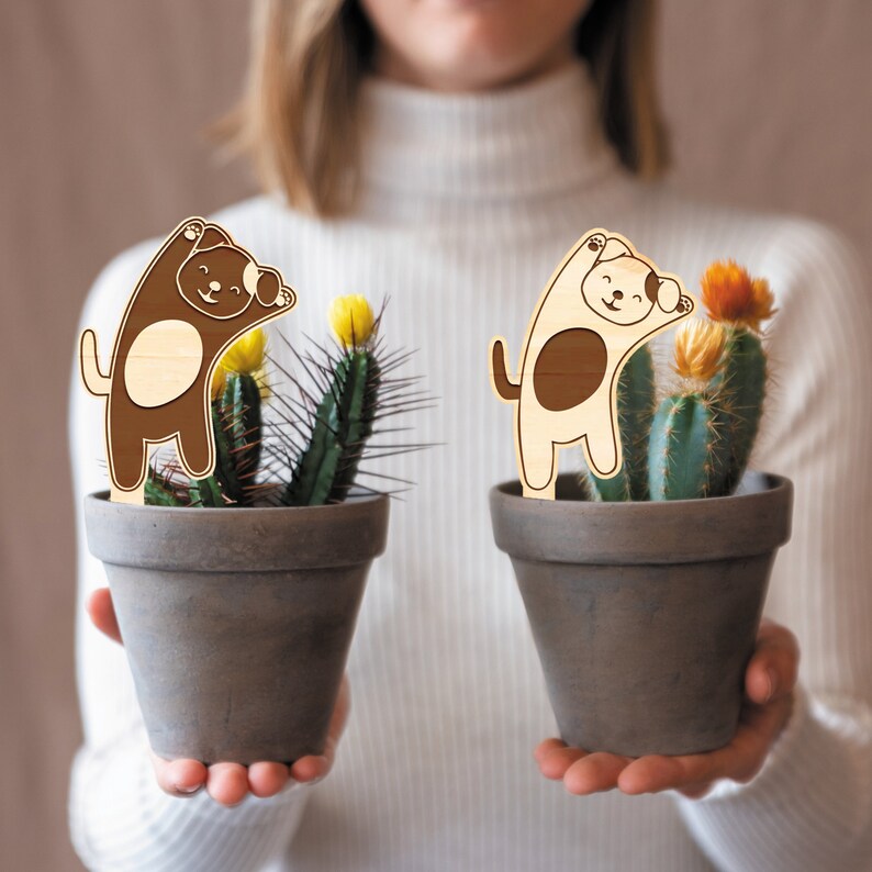 May include: Two brown terracotta pots with cactus plants and wooden dog figurines. The dogs are brown and white with black eyes and are in a playful pose.