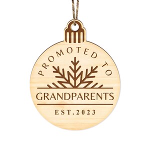 May include: A wooden Christmas ornament shaped like a circle with the text "Promoted to Grandparents Est. 2023" and a snowflake design.
