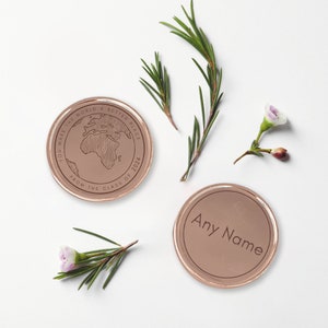 May include: Two round, copper-colored tokens. One token features a world map with the text "You make the world a better place from the class of 2024". The other token has the text "Any Name" in a simple font.