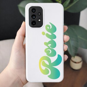 May include: White phone case with a gradient green and yellow cursive text that reads "Rosie". The phone case has a camera module on the upper left corner.