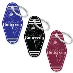 May include: Three keychains with a motel key design. Each keychain features a white outline of a flower with the text "Buckle Up Buttercup" in white lettering. The keychains are blue, black, and burgundy.