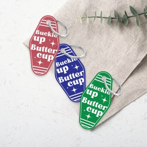 May include: Three keychains shaped like motel room keys with the text "buckle up butter cup" in white on a red, blue, and green background.