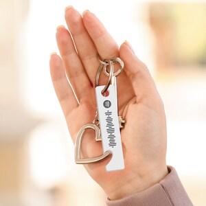 May include: A silver keychain with a white rectangular tag featuring a black and white barcode and the Spotify logo. The keychain also includes a silver heart charm.