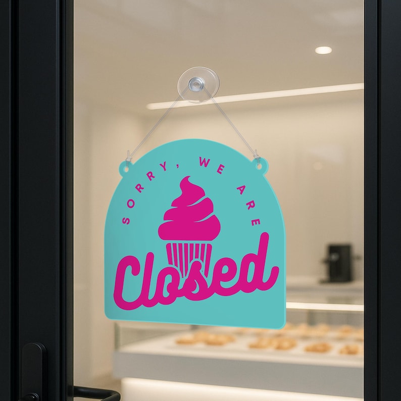 Może przedstawiać: Turkusowy znak z r&oacute;żową grafiką babeczki i napisem "Closed" w kursywie. Znak wisi na szklanych drzwiach, wskazując, że firma jest nieczynna.