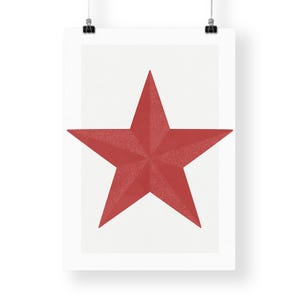May include: A red five-pointed star on a white background, printed on a poster. The star has a textured appearance and is centered on the poster. The poster is hanging from two black clips.