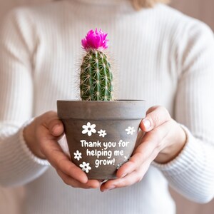 May include: A small cactus plant in a terracotta pot with the text "Thank you for helping me grow!" and white flower graphics.