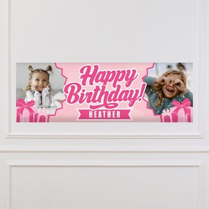 May include: A pink birthday banner with the words "Happy Birthday!" in a cursive font. The name "Heather" is below the text. The banner has photos of a young girl on each side, with pink gift boxes.