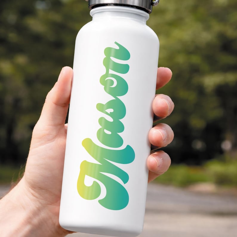 May include: White water bottle with a silver lid, featuring the name "Mason" in a gradient of yellow and teal. The bottle is held by a hand, with a blurred green background.