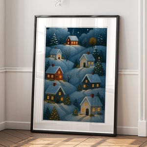 May include: A framed print of a winter village scene. Snow-covered hills feature several houses with lit windows and chimneys. Evergreen trees and a starry night sky complete the cozy, festive illustration.