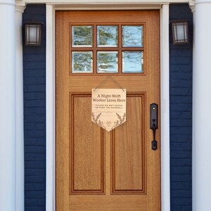 May include: Wooden sign hanging on a wooden door. The sign reads "A Night Shift Worker Lives Here. Please do not knock or ring the doorbell." The sign has a heart and floral design.