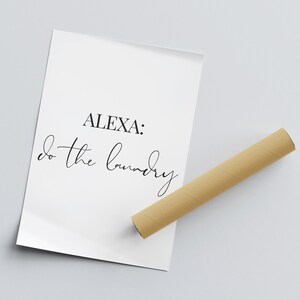 May include: A white poster with black text that reads "ALEXA: do the laundry". The poster is rolled up and sitting on a light gray surface.