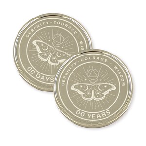 May include: Two silver-colored recovery coins. Each coin features a moth design with the words "SERENITY - COURAGE - WISDOM" around the edge. One coin reads "00 DAYS" and the other reads "00 YEARS".