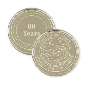 May include: Two silver-colored coins with a beige background. The first coin has the text "00 Years" in a circle. The second coin has a design of a moon, stars, and waves with the text "Make the comeback... stronger than the setback."