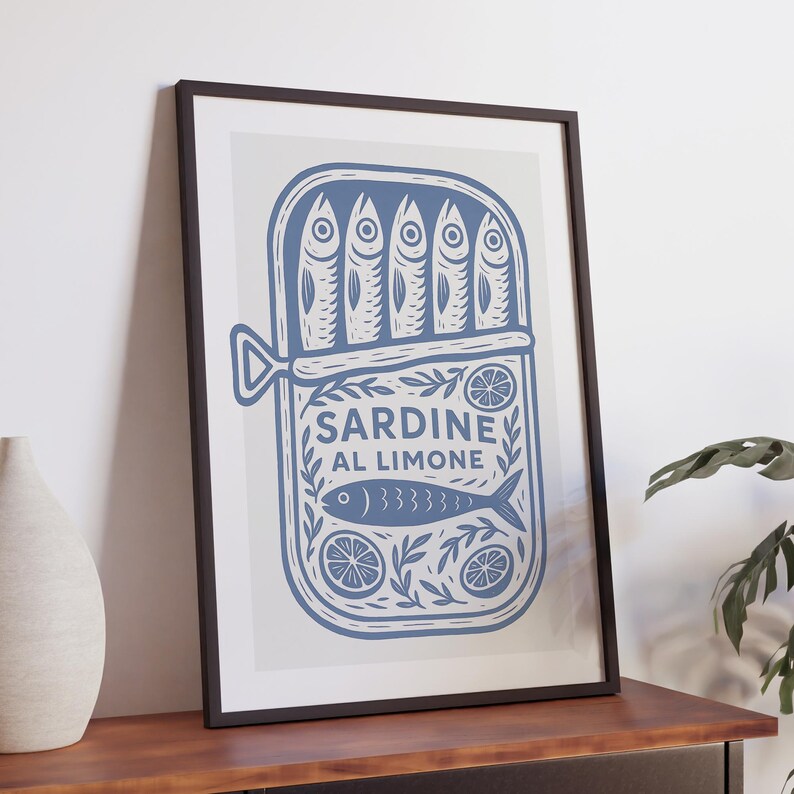 May include: A framed print featuring a blue illustration of a sardine can with the text "SARDINE AL LIMONE." The design includes stylized fish, lemon slices, and decorative foliage, set against a light gray background.