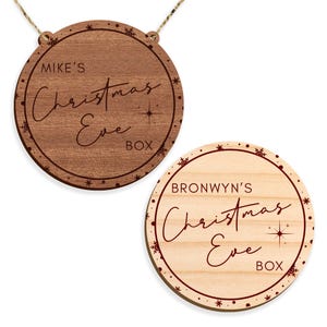 May include: Two round wooden Christmas Eve boxes with red lettering and snowflakes. The top box says "Mike's Christmas Eve Box" and the bottom box says "Bronwyn's Christmas Eve Box".