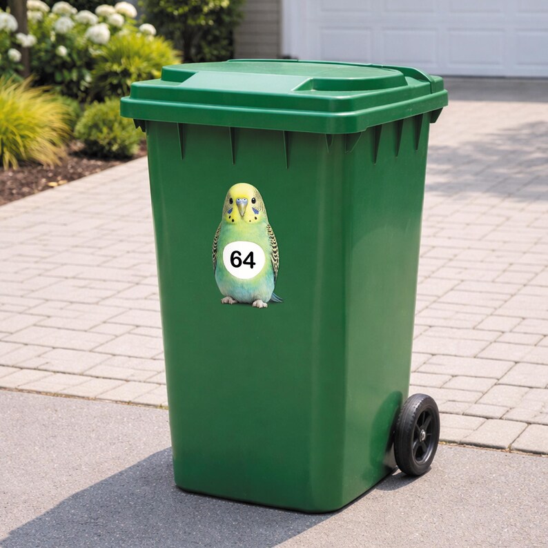May include: A green outdoor trash can with a matching lid and black wheels. A sticker of a colorful parakeet with the number 64 is affixed to the front of the can. The can is on a paved surface with greenery in the background.