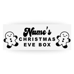May include: A white rectangular sign with black text reading "Name's CHRISTMAS EVE BOX." Two gingerbread man figures are on either side of the text. The gingerbread men have smiling faces and button details.