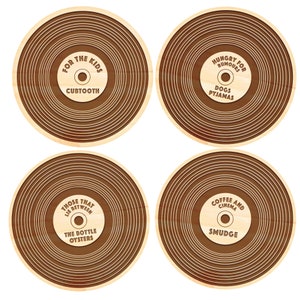 May include: Four wooden coasters with a record-like design. Each coaster features a different phrase and design. The first coaster says "For the Kids" with the word "Cubtooth" underneath. The second coaster says "Hungry for Rumours" with the words "Dogs Pyjamas" underneath. The third coaster says "Those That Lie Between The Bottle Oysters". The fourth coaster says "Coffee and Cinema" with the word "Smudge" underneath.