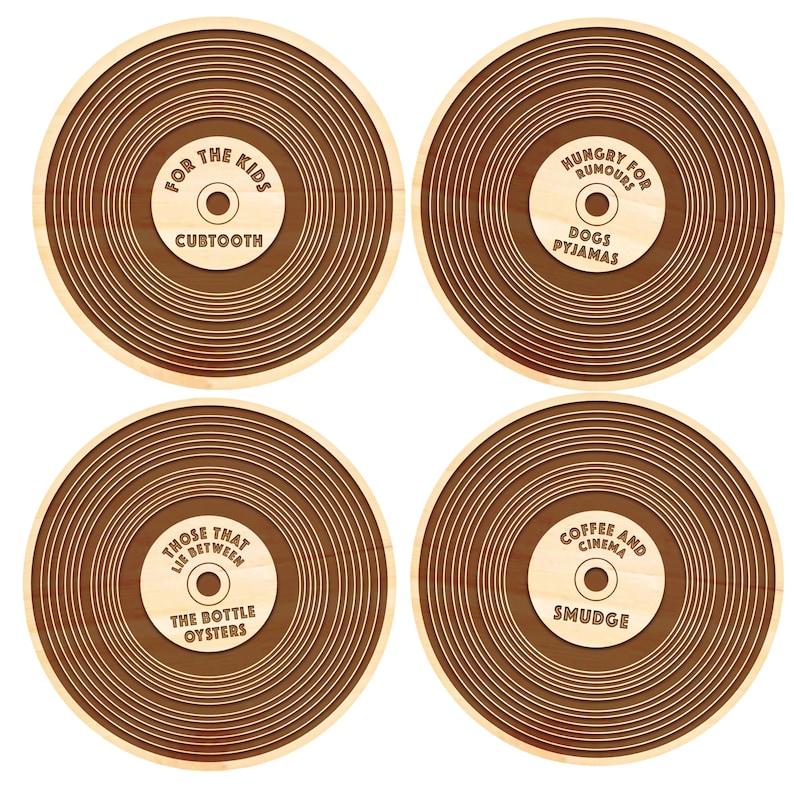 May include: Four wooden coasters with a record-like design. Each coaster features a different phrase and design. The first coaster says "For the Kids" with the word "Cubtooth" underneath. The second coaster says "Hungry for Rumours" with the words "Dogs Pyjamas" underneath. The third coaster says "Those That Lie Between The Bottle Oysters". The fourth coaster says "Coffee and Cinema" with the word "Smudge" underneath.